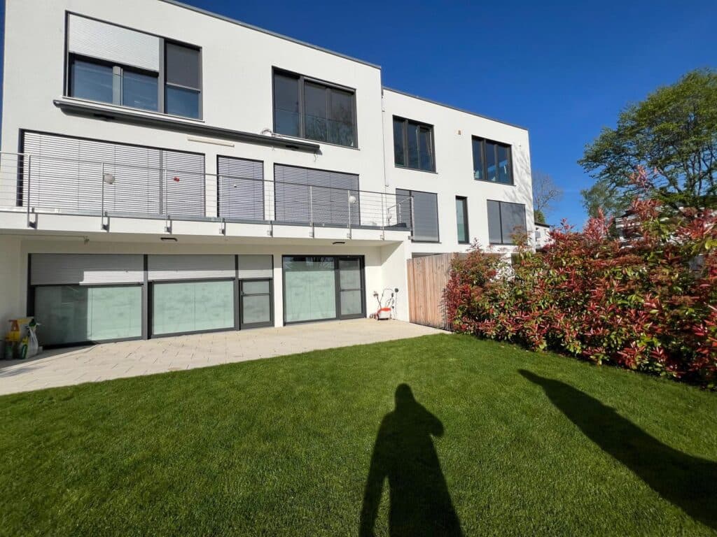 Rückseite eines Mehrfamilienhauses mit weiß verputzter Fassade, Balkonen und gepflegtem Garten